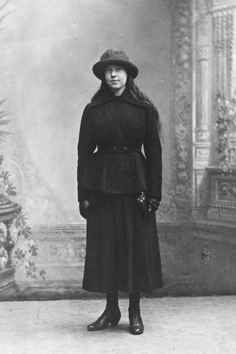 Ung flicka i svart kjol, kappa och hatt.
