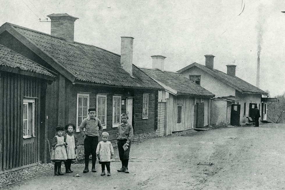 svart vit bild gata kantad av låga hus, fem barn på gatan tittar in i kameran.