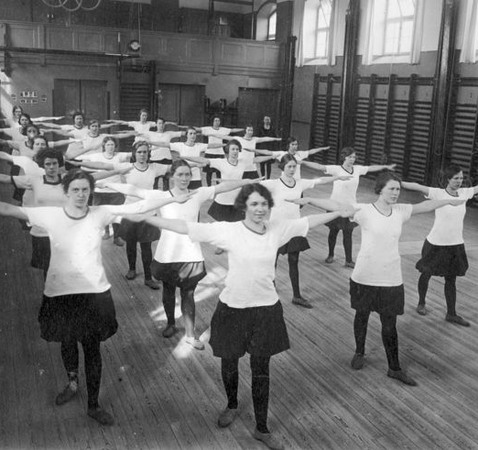 Unga flickor med armarna utsträckta på rad i en gymnastiksal.