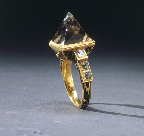 Ring av guld, dekorerad med svart emalj. I mitten en pyramidformig, ljus rökkvarts