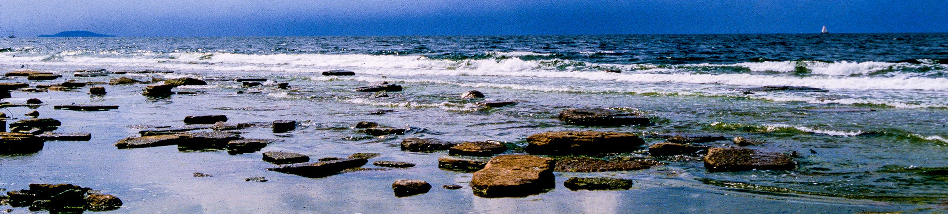 Stenig strand med lugnt vatten i förgrunden