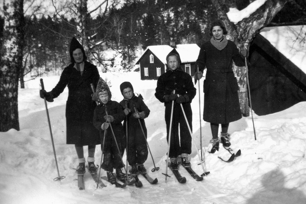 Svartvitt foto med barn och vuxna på skidor i snö.