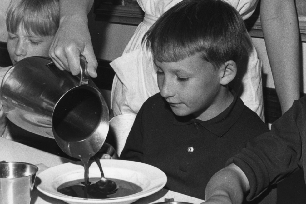 Svartvitt foto, barn serveras saftsoppa från metallkanna.