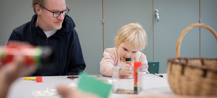Man i glasögon ser på när flicka koncentrerat tar limstift på papper