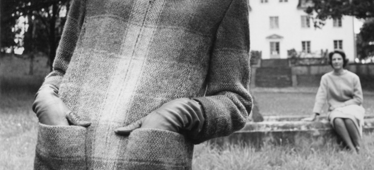 svartvitt foto, i förgrunden kvinna i kappa, i bakgrunden kvinna sitter på kanten av en fontän 