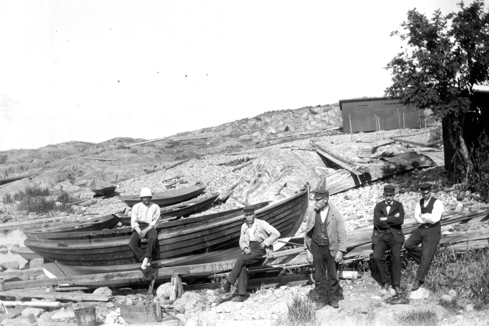 Flera män vid båtar i skärgårdslandskap med klippor.