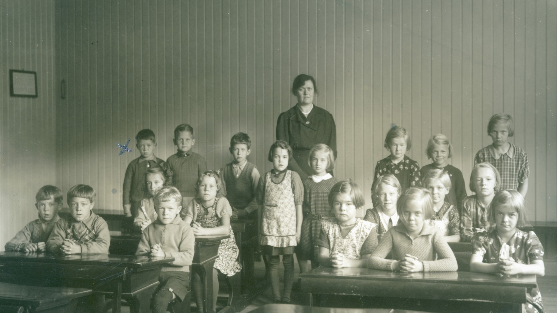 En skolklass med barn sitter vid bänkarna med knäppta händer. 
