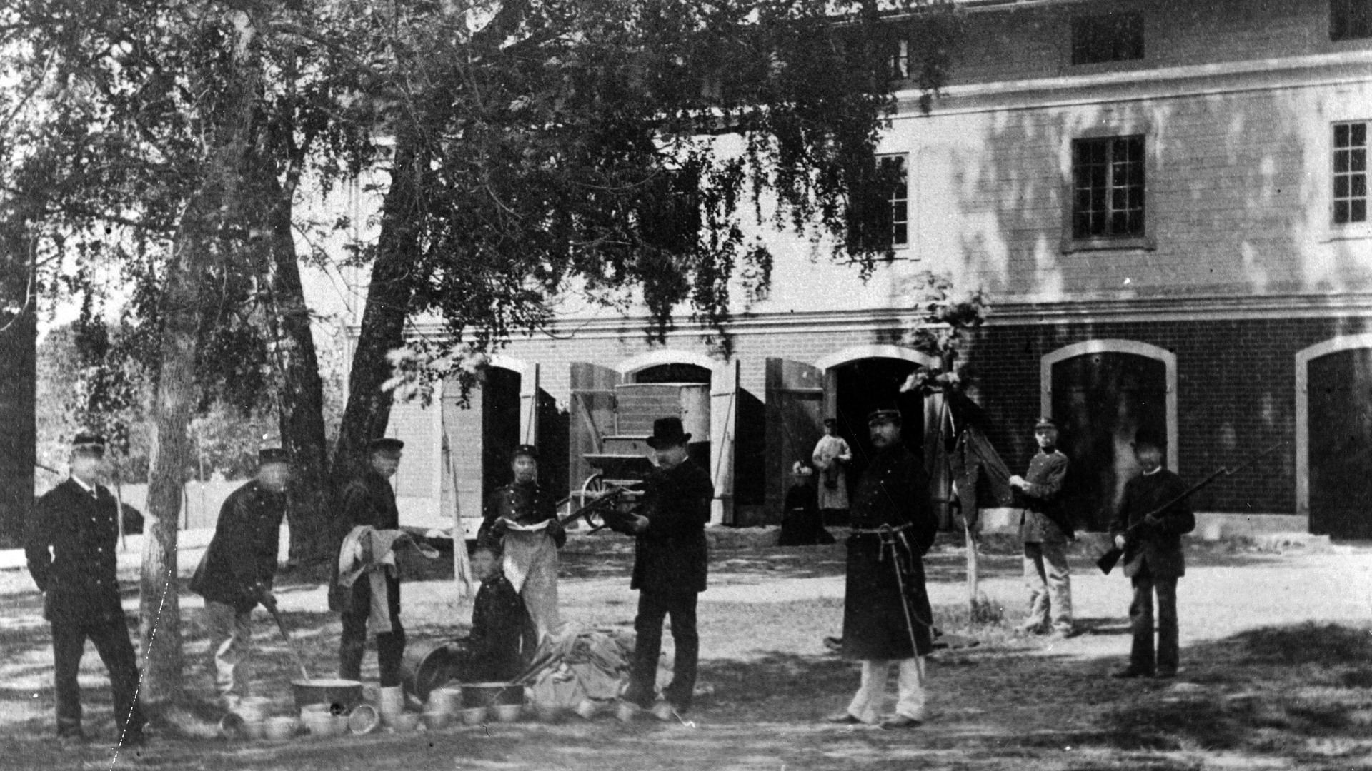 En grupp män står under en björk framför ett hus.