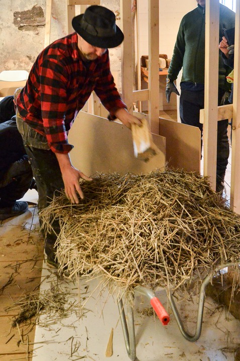 En man lägger lerhalmblandningen emellan två träskivor.