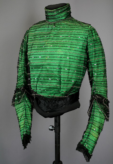 Klänningsliv av grönt siden överklätt med svart tyll dekorerad i ränder med paljetter och stenkolspärlor. 