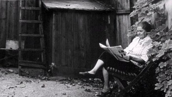 Kvinna läser en tidning utomhus på en stadsgård.