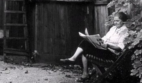 Kvinna kopplar av med tidning på innergård.