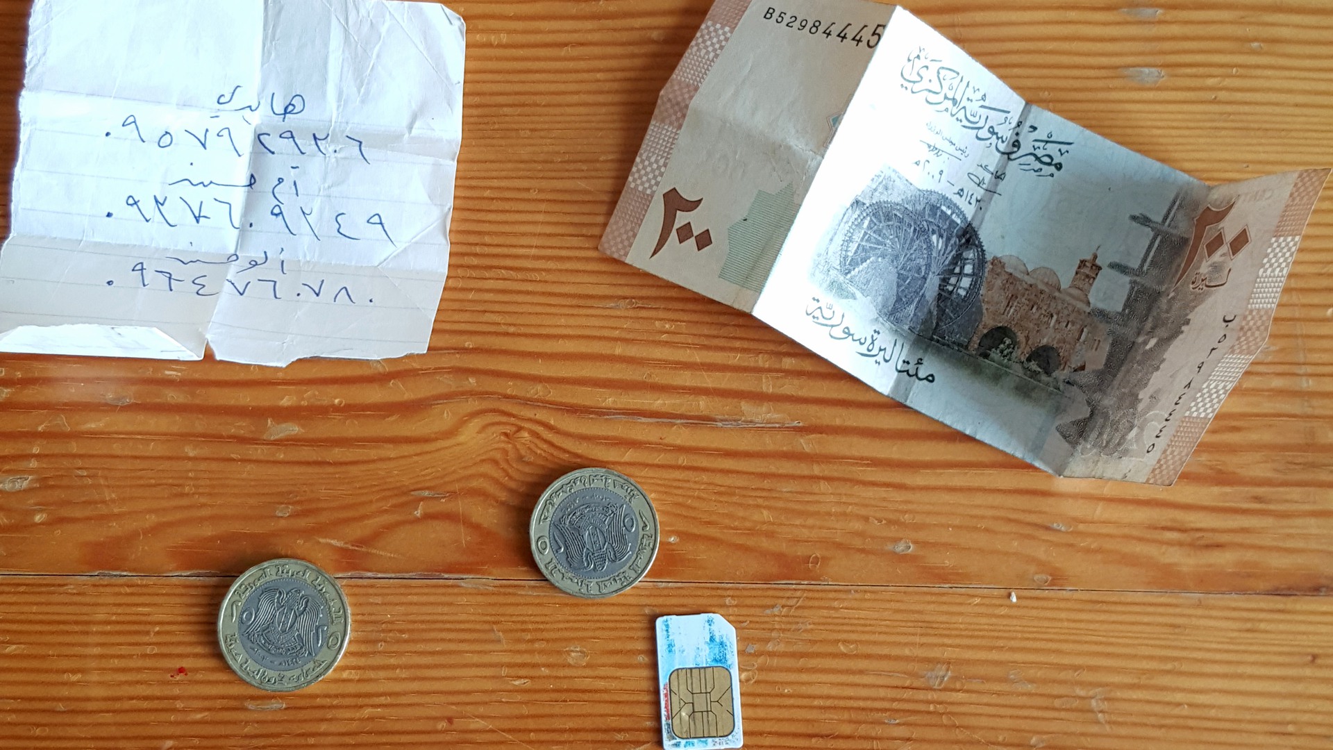 Mynt och sedlar från Syrien, papperslapp med arabiska tecken och ett SIM-kort. 