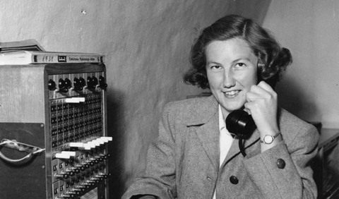 Kvinna sitter vid ett skrivbord och håller i en telefonlur