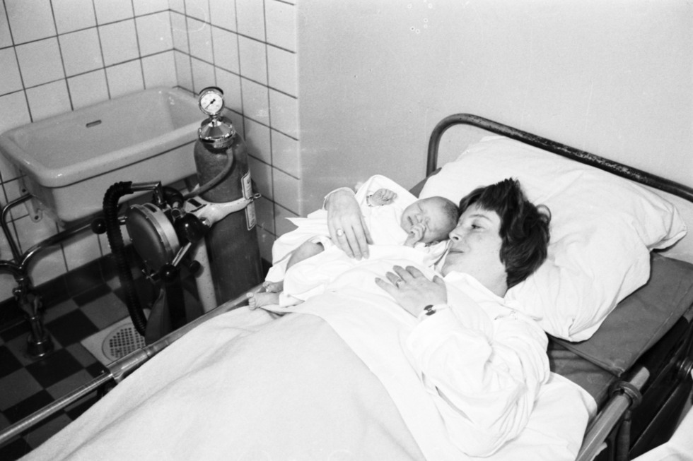 Mamma och barn vilar i en säng, en tub med lustgas står jämte.