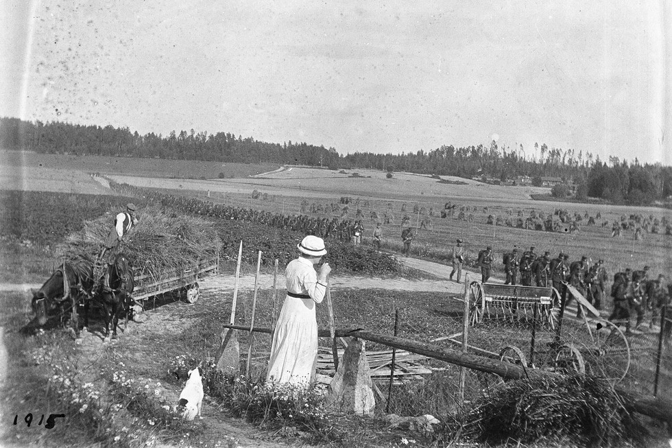 En kvinna vid höskörden ser på soldater som marscherar förbi.