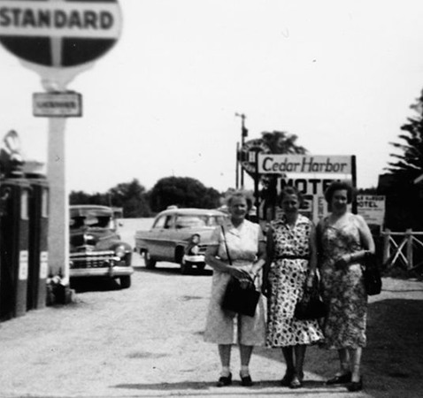 Tre kvinnor i klänningar framför skyltarna "Cedar Harbor" och "Standard".