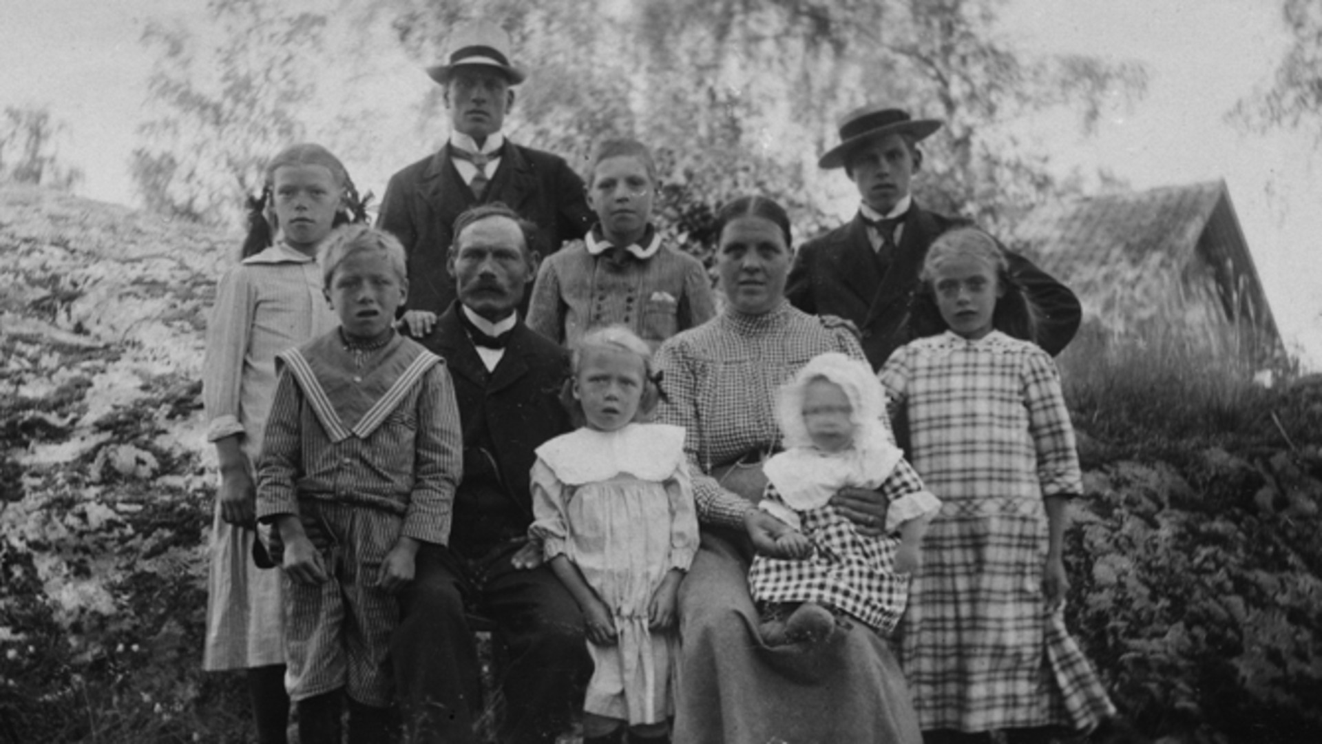 En man och en kvinna sitter bredvid varandra, omgivna av åtta barn i olika åldrar.