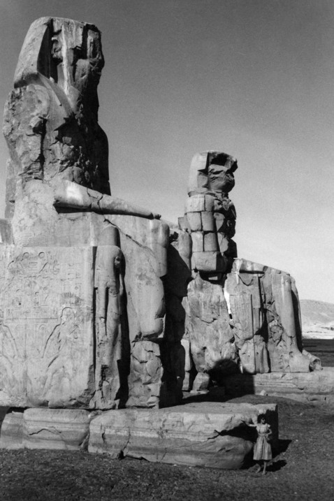 En kvinna står vid foten av två jättelika skulpturer av två personer som sitter rakryggade bredvid varandra.