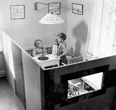 En flicka och en pojke leker i ett pyttelitet låtsas-kök, bakom en rumsavdelare.