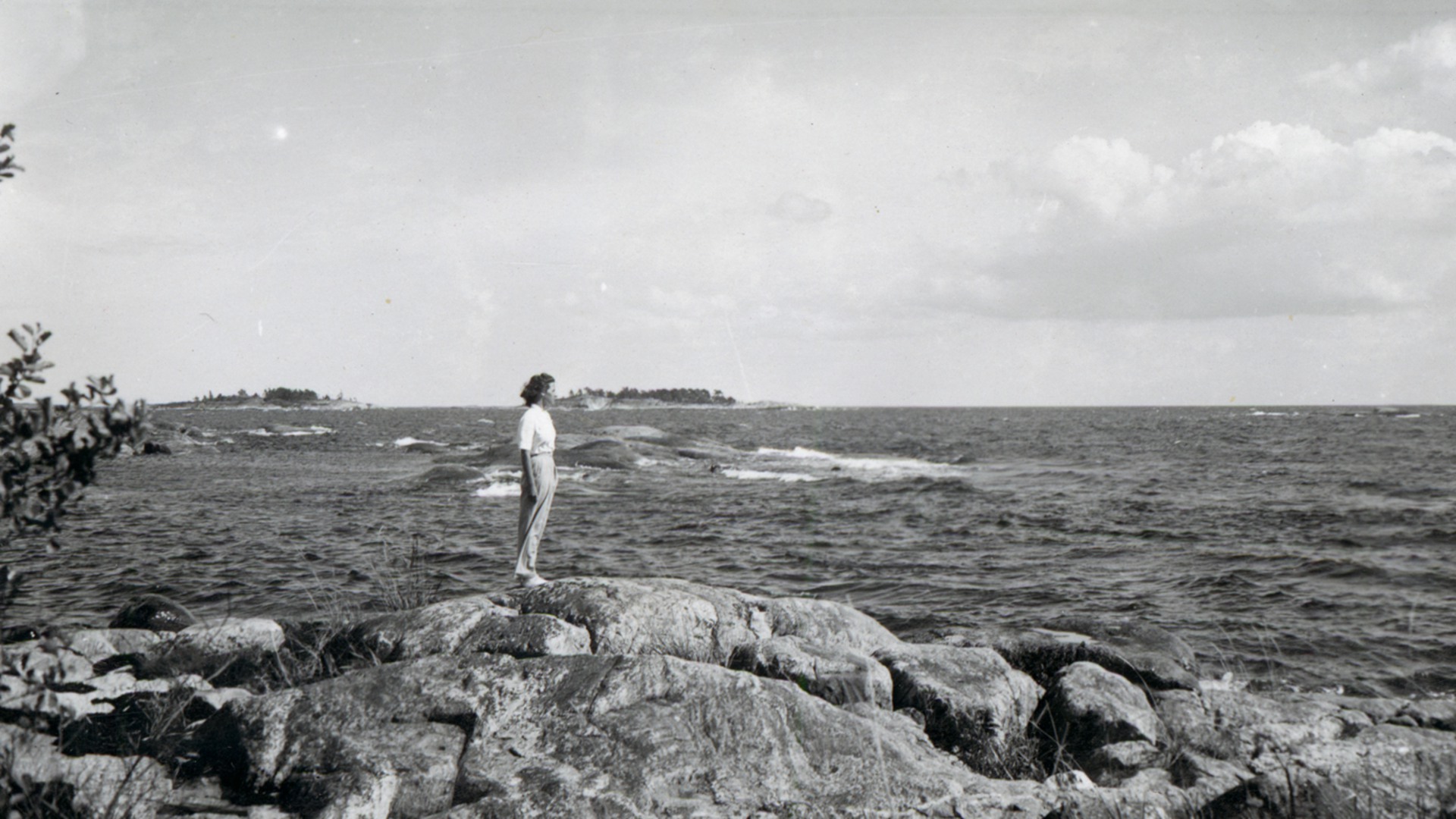 En kvinna står i skärgården och tittar på havet.