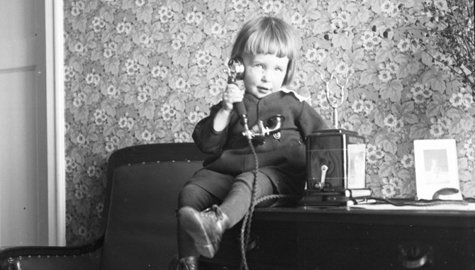 Svartvitt fotografi av liten flicka som pratar i telefon, ca 1930tal.