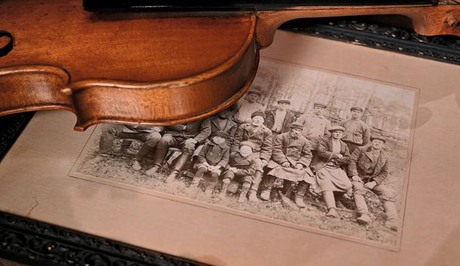 Fiol liggandes över kanten av ett inramat grupporträtt med lantarbetare 1915.