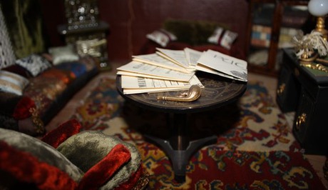 Detalj från ett av rummen i dockskåpet, ett bord med tidningar och en pipa.