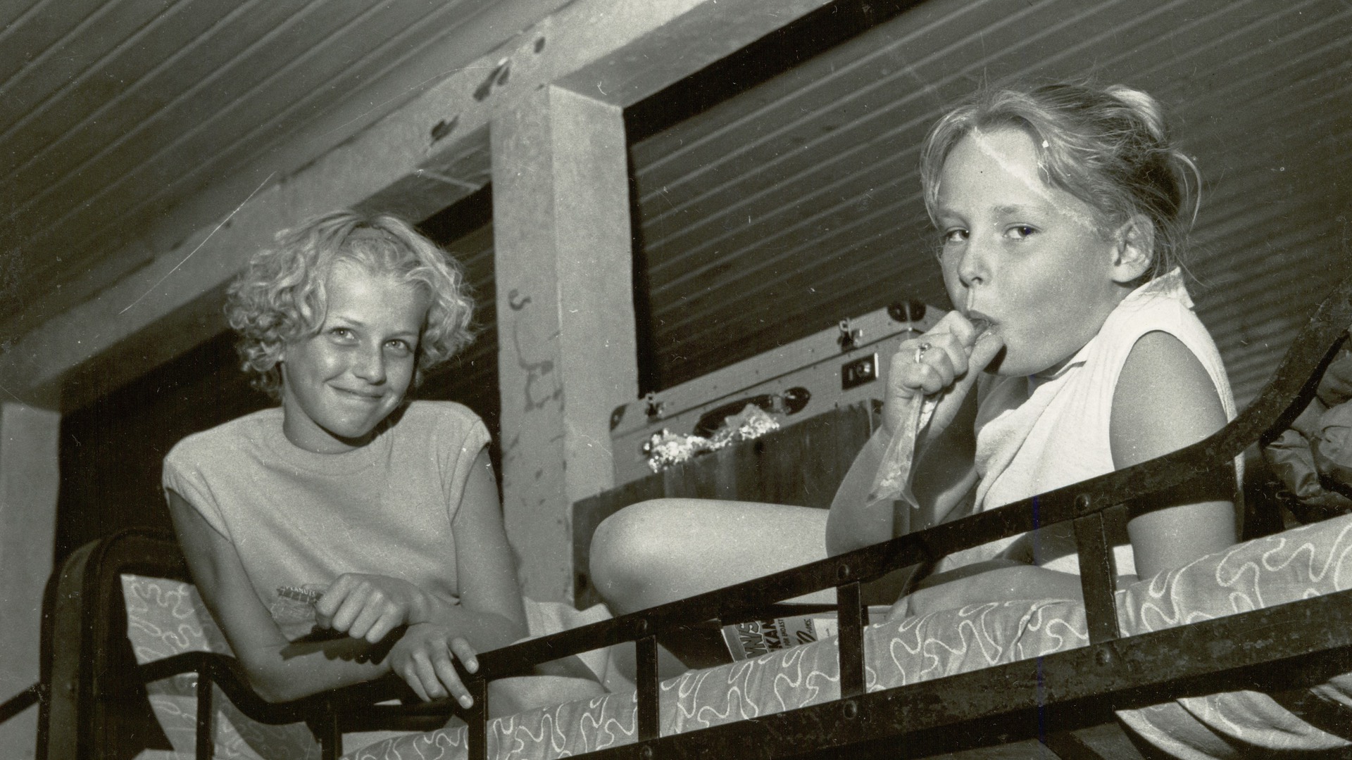 Två flickor i en våningssäng, en av dem äter glass.