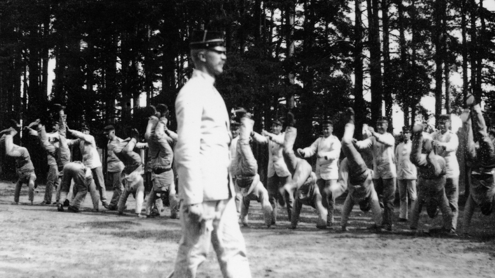 En man leder gymnastikövningen, i bakgrunden syns tränande soldater.