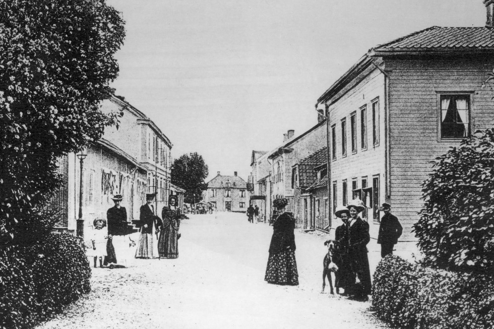 En gata i Malmköping, på båda sidor syns hus och människor.