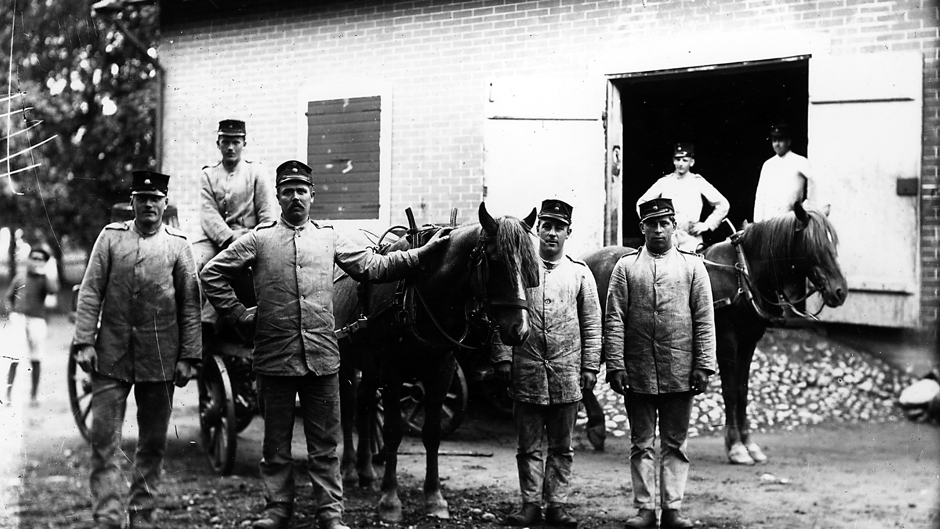 Några män står med två hästar och en vagn framför ett proviantmagasin. 