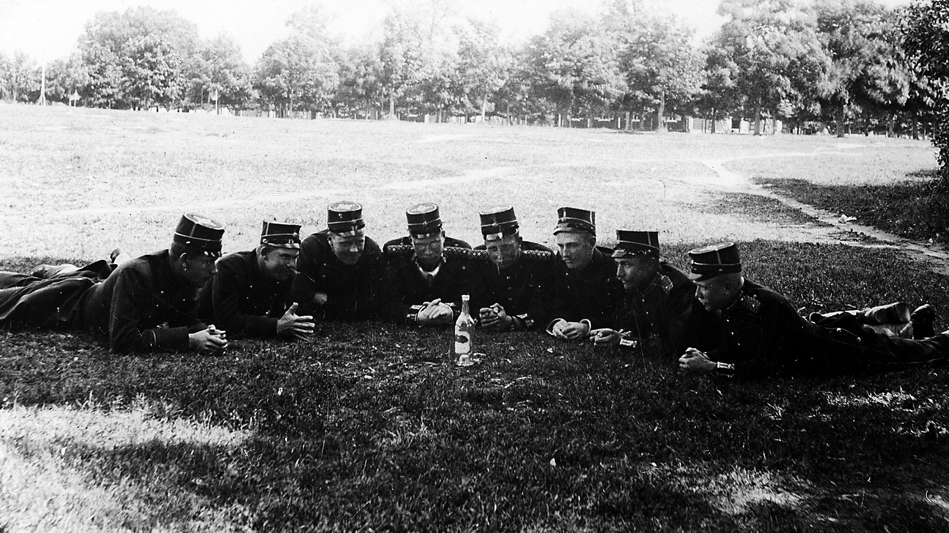 En grupp soldater som ligger på gräsmattan runt en flaska. 