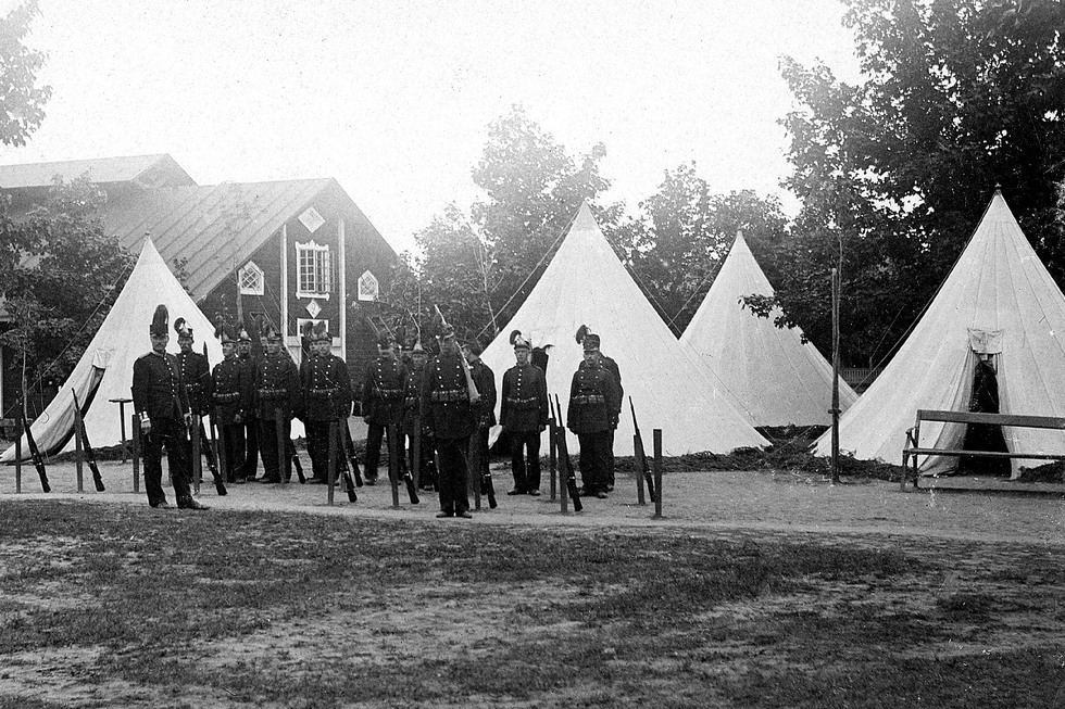 En grupp soldater framför fyra vita tält.