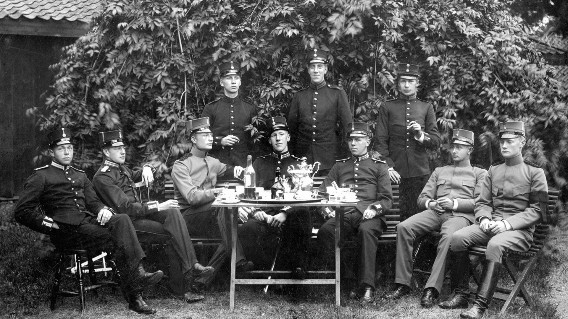 Soldater sitter ute i trädgården runt ett dukad bord.