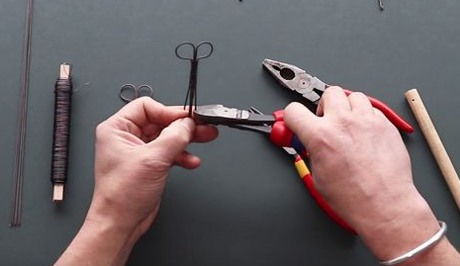 Ett par händer böjer en ståltråd med hjälp av en tång.